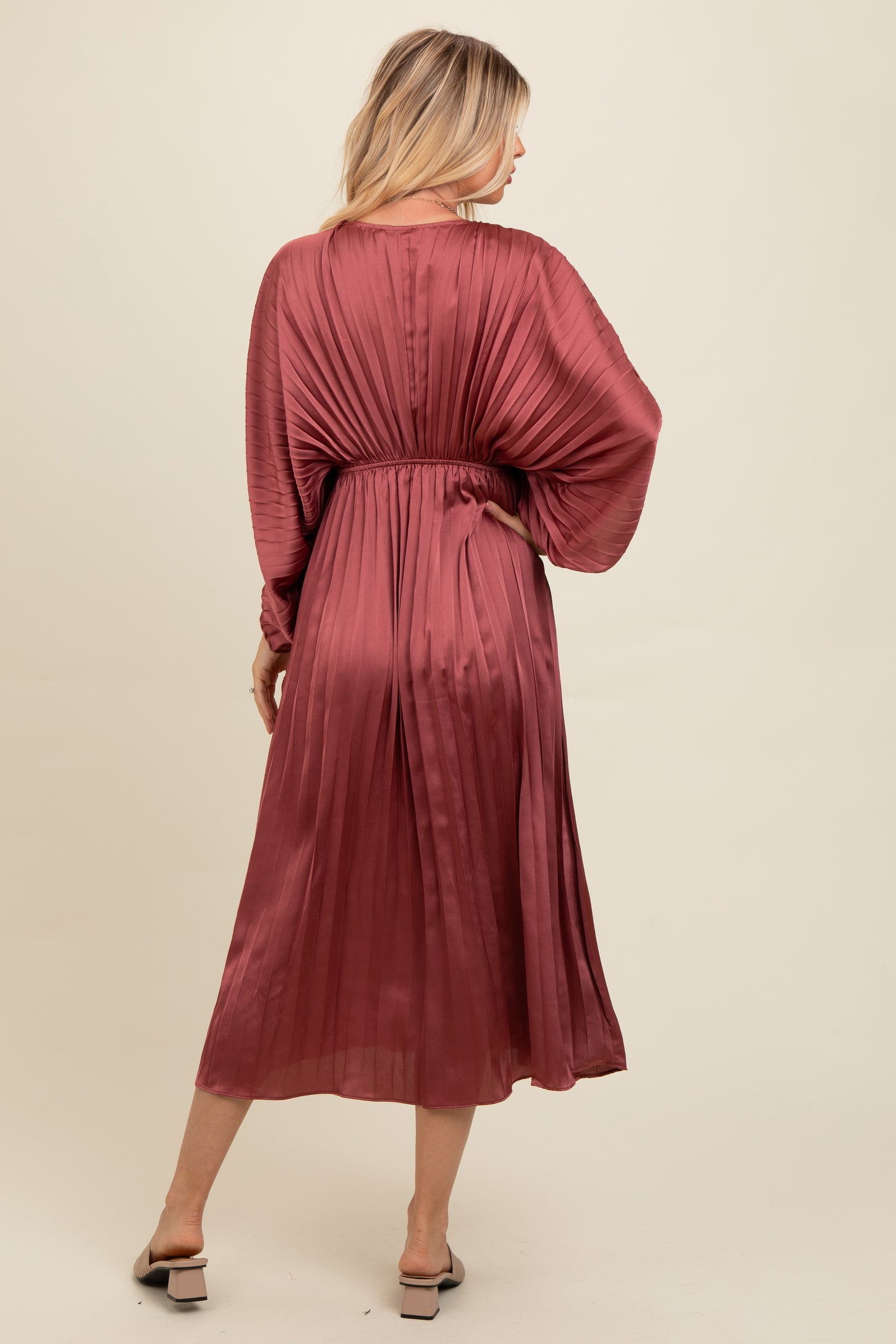 woman wearing a dusty rose pleated midi dress with a cinched waist and balloon sleeves, viewed from the back