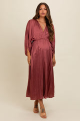 woman wearing a rust colored pleated maternity dress with a deep v-neck and a baby bump visible