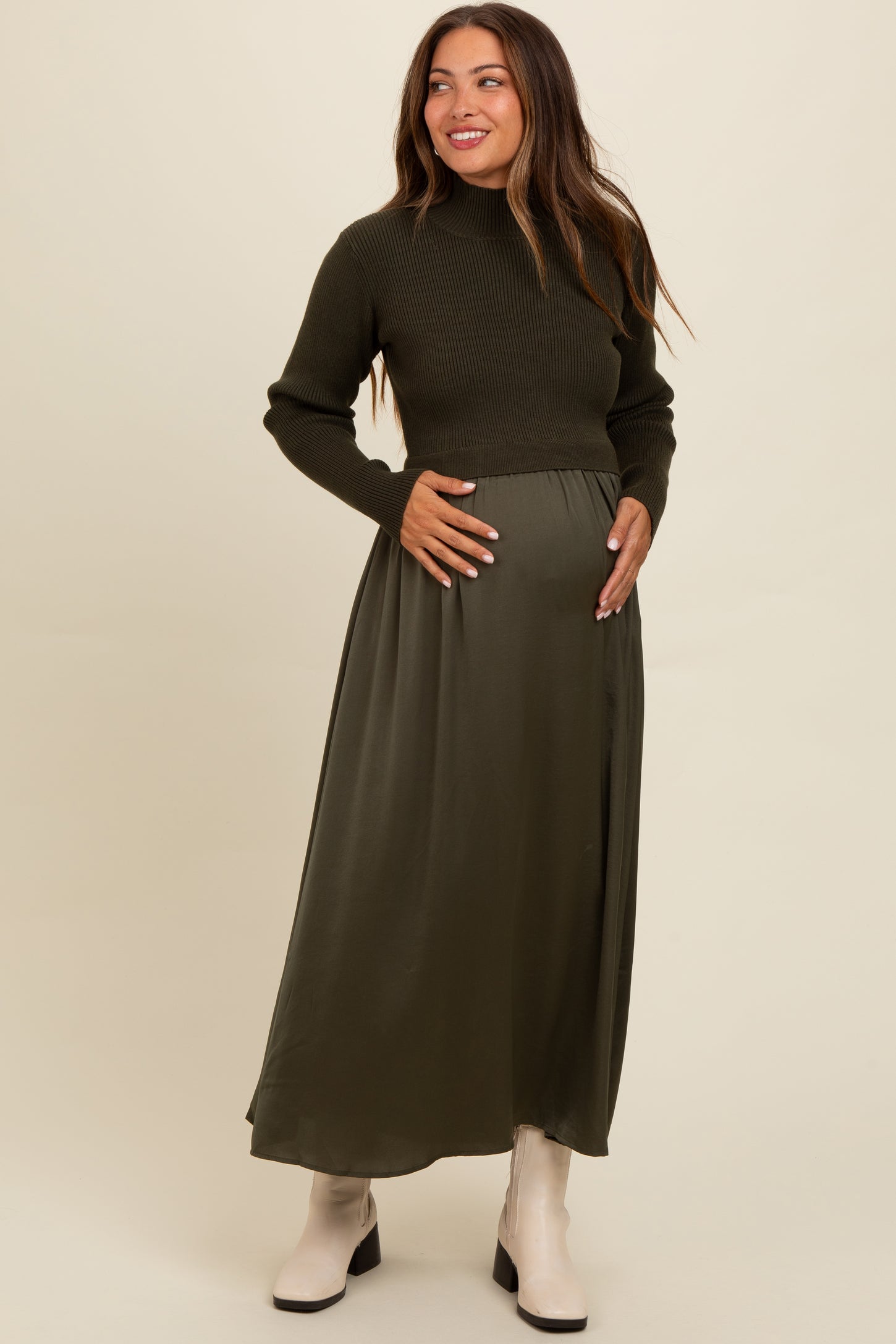 woman wearing a dark green long sleeve maternity dress and a fitted sweater, holding her baby bump