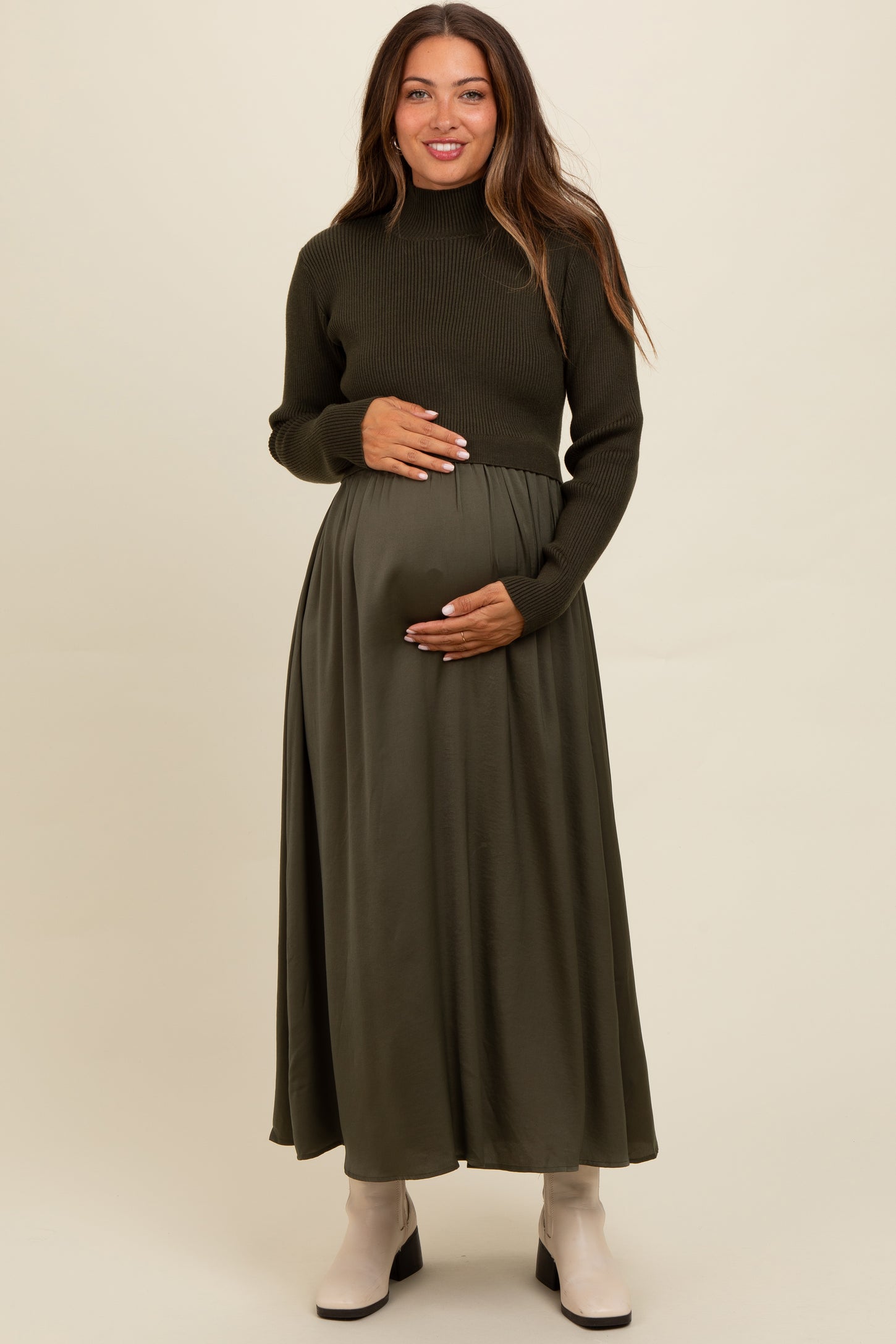 woman wearing a dark green maternity long sleeve sweater and a flowy skirt, holding her baby bump