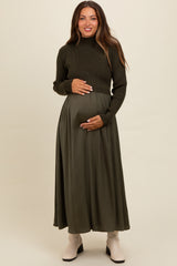 woman wearing a dark green maternity long sleeve sweater and a flowy skirt, holding her baby bump