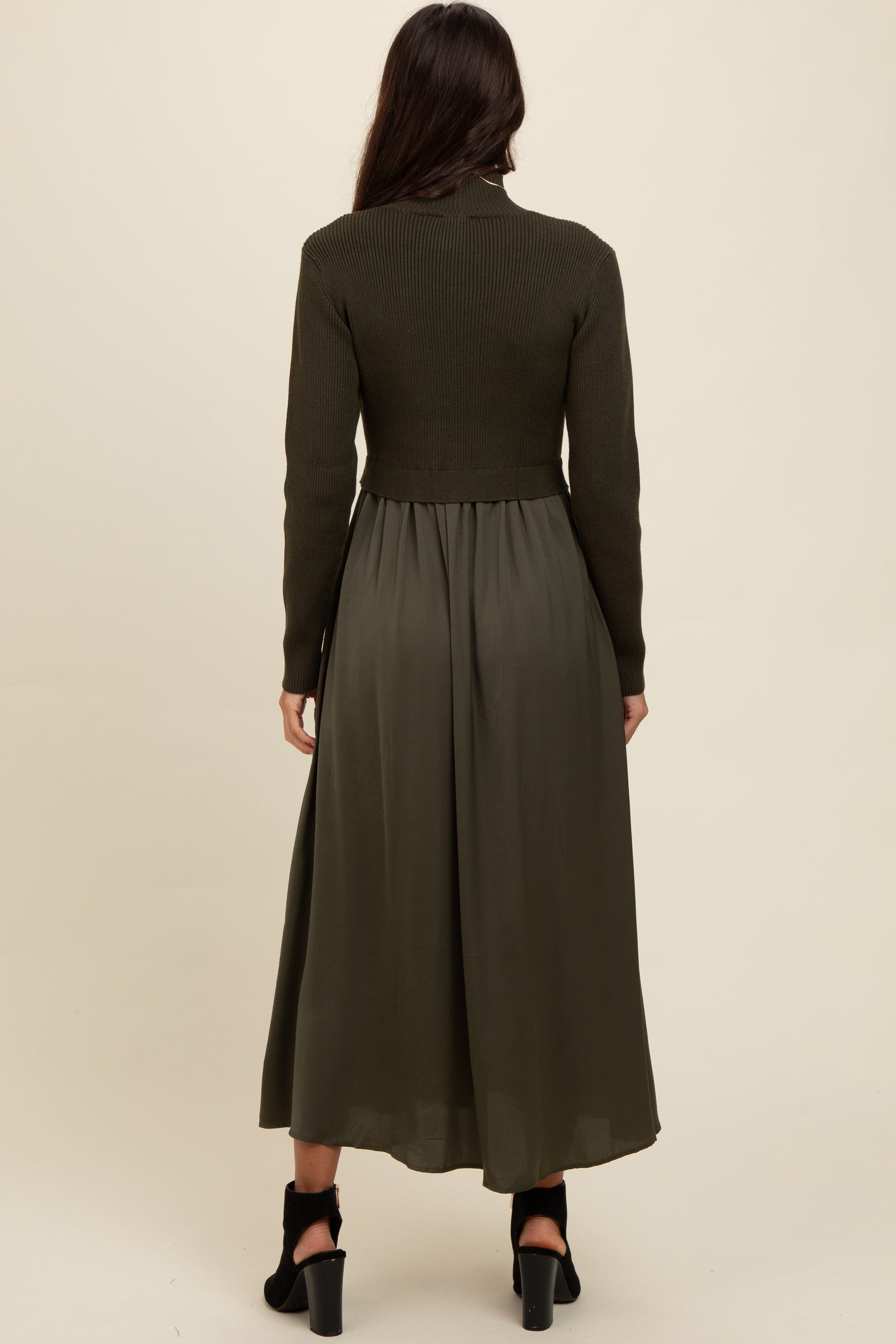 woman wearing a long olive green ribbed knit and satin dress with a fitted bodice and flowy skirt, viewed from the back