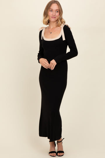 woman wearing a black long sleeve maxi dress with a beige scoop neckline and bow details on the shoulders