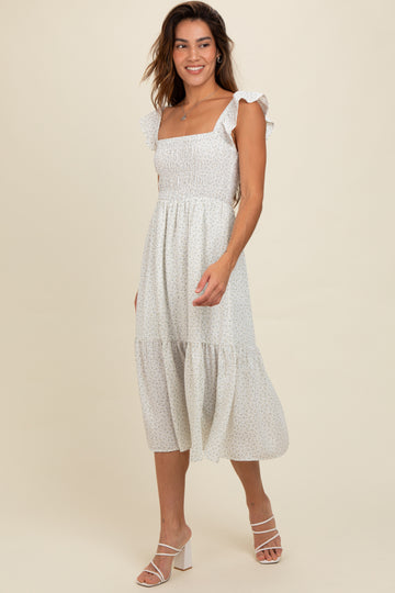 woman wearing a white floral midi dress with ruffle sleeves and a smocked bodice, walking on a plain background