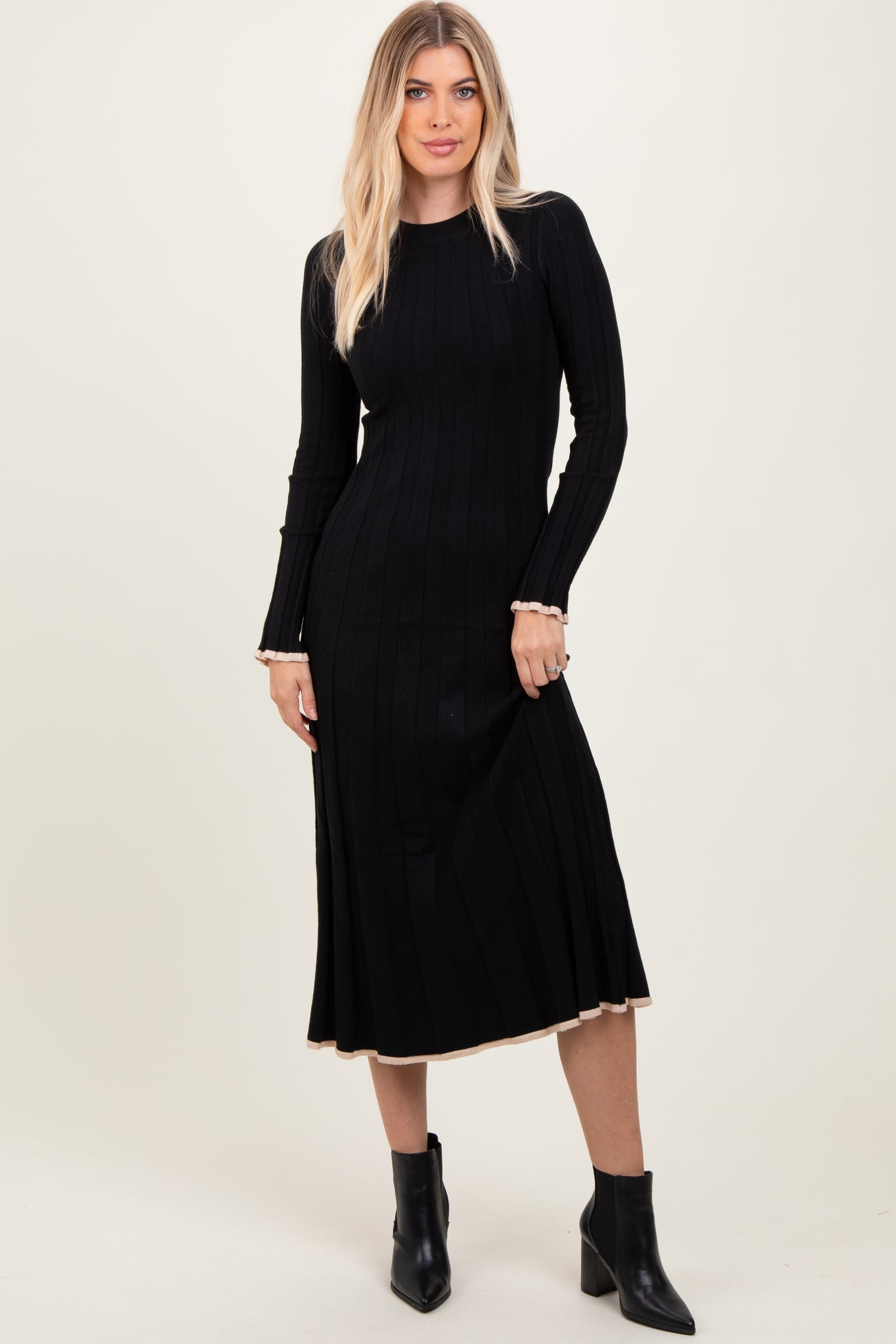 woman wearing a black ribbed knit long sleeve dress with a fitted silhouette and contrasting hemline, paired with ankle boots