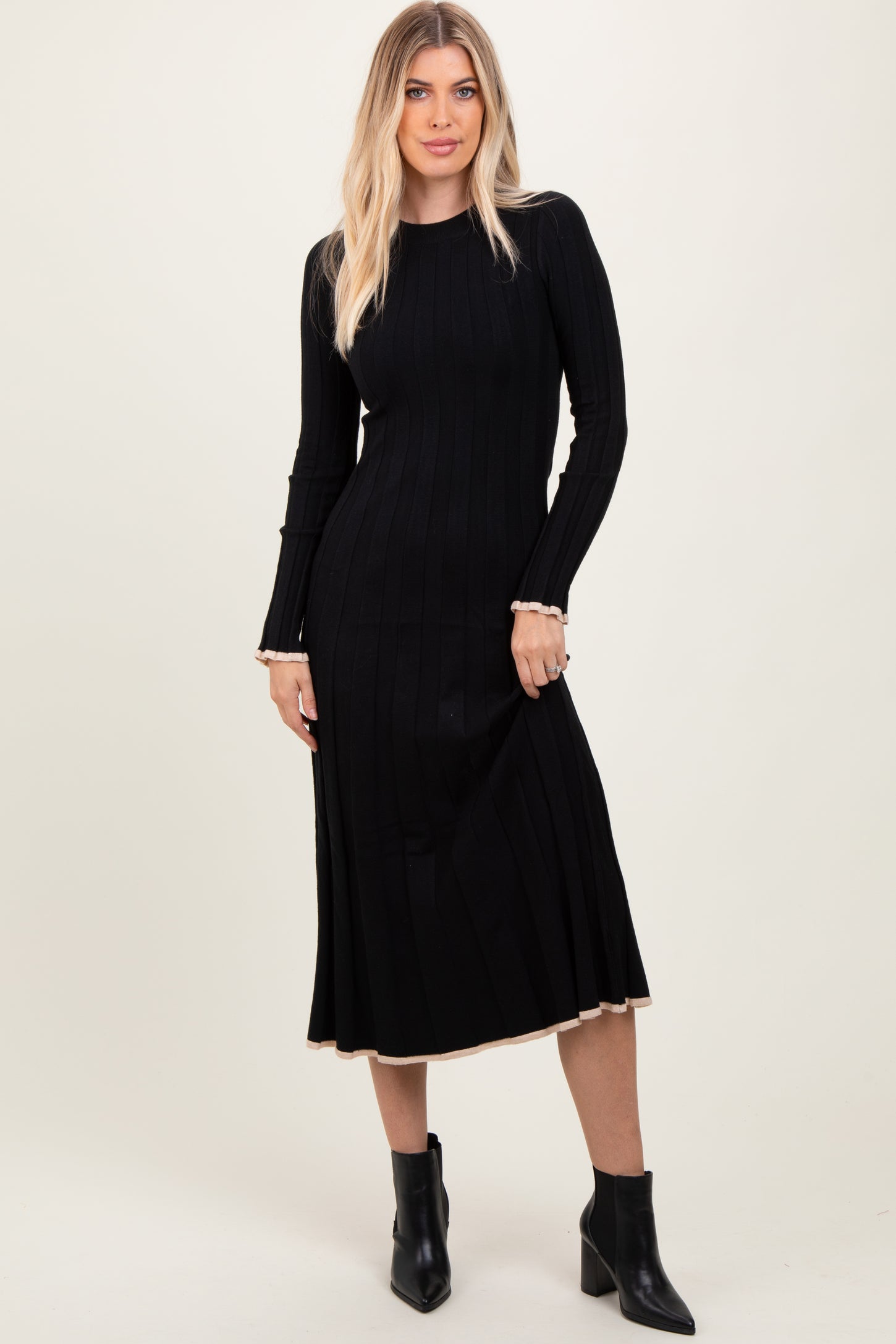 woman wearing a black ribbed knit long sleeve dress with a fitted silhouette and contrasting hemline, paired with ankle boots