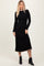 woman wearing a black ribbed knit long sleeve dress with a fitted silhouette and contrasting hemline, paired with ankle boots