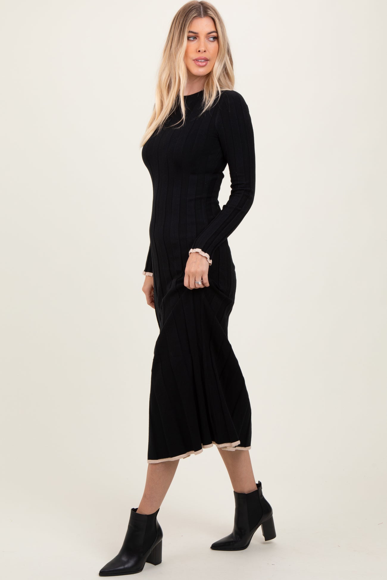 woman wearing a black ribbed midi dress with long sleeves and a scalloped hem, paired with black ankle boots