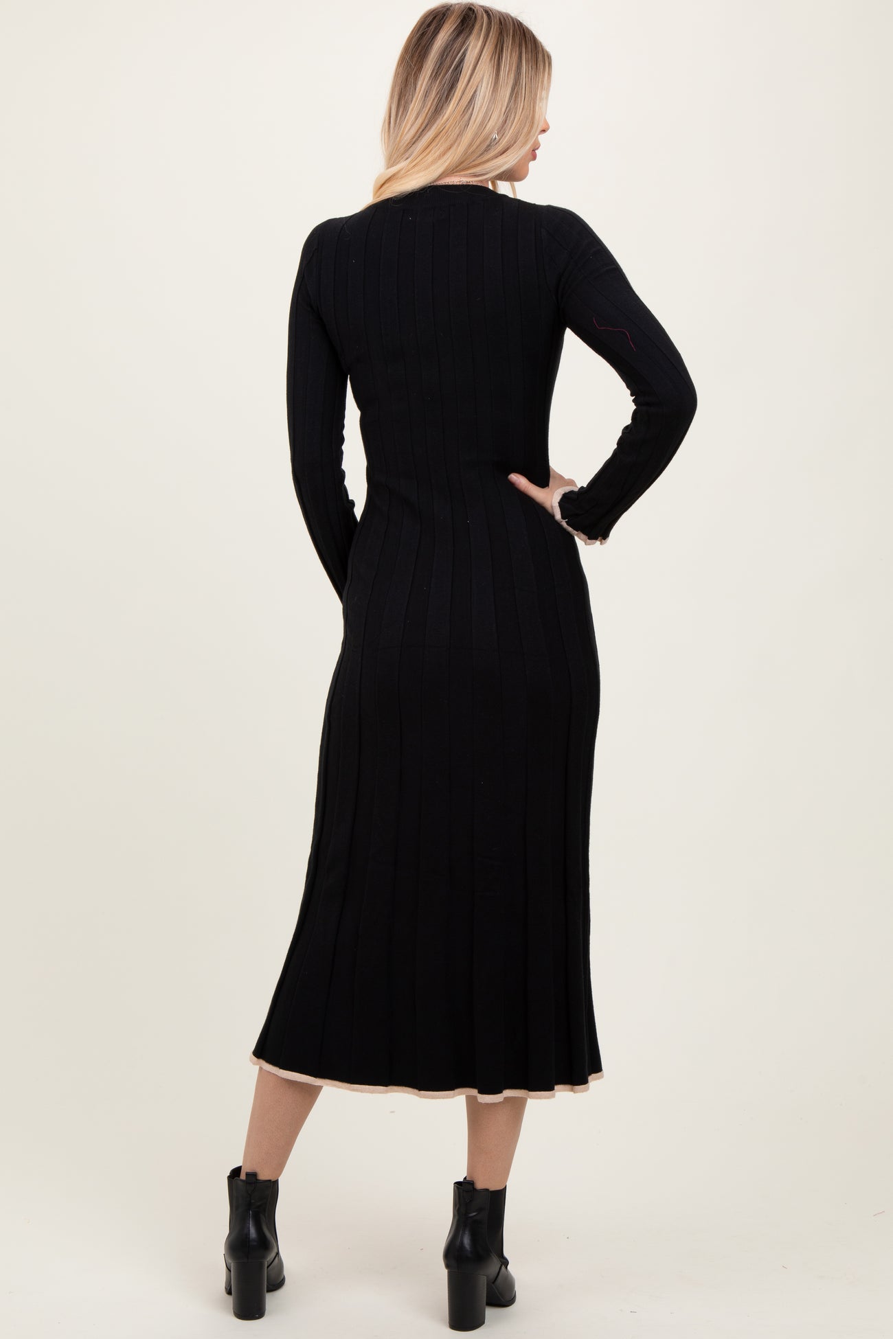 woman wearing a black ribbed knit midi dress with long sleeves and a flared hem, viewed from the back