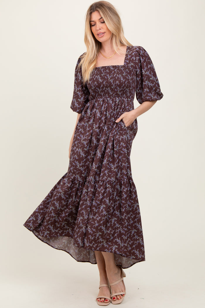 woman wearing a brown floral maxi dress with puff sleeves and a square neckline, standing with hands in pockets