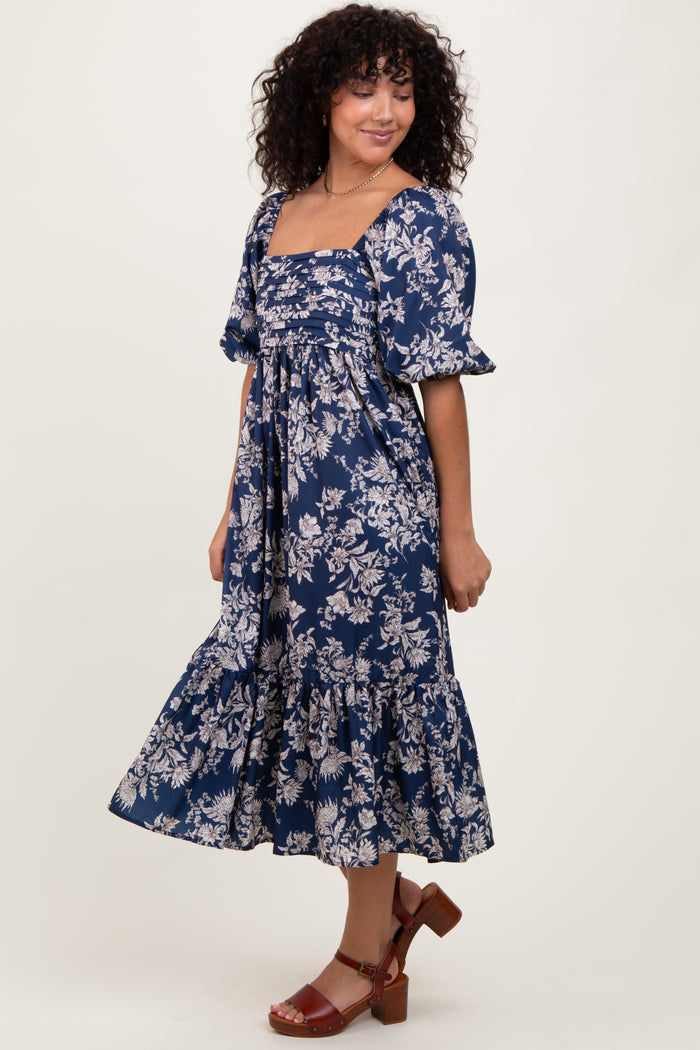 woman wearing a navy blue floral midi dress with puff sleeves and a tiered skirt, smiling and standing in profile