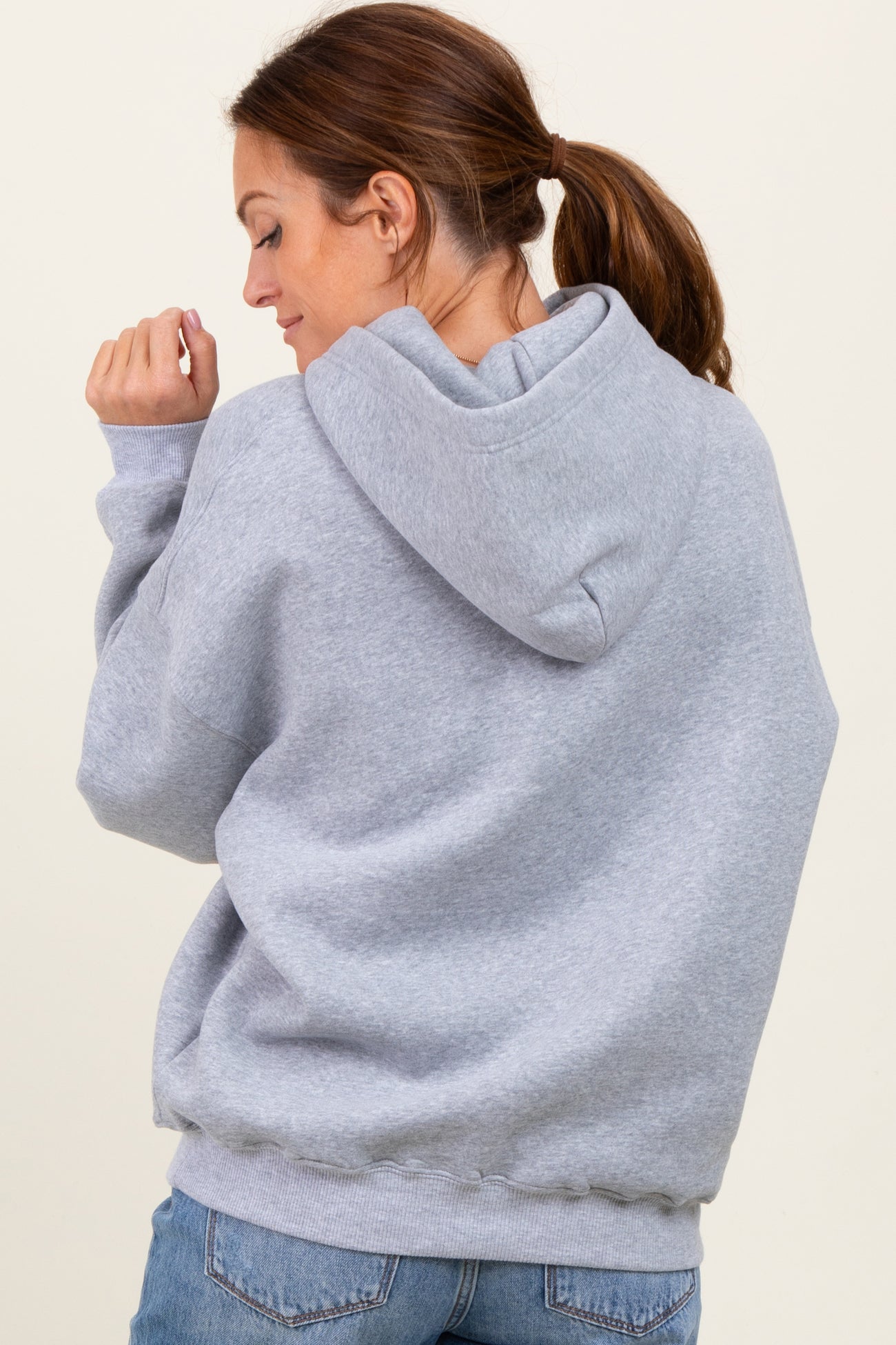 woman wearing a light gray oversized hoodie from the back with a hood and long sleeves