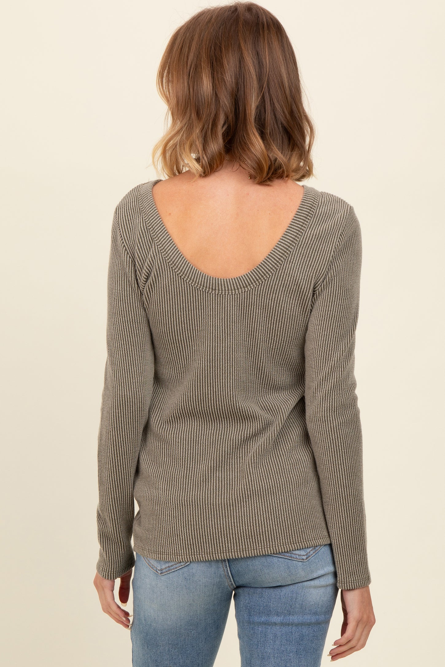 woman wearing a light olive ribbed long sleeve top with a scoop back and styled with blue jeans