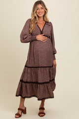 woman wearing a brown floral maternity dress with long sleeves and tiered skirt, holding her baby bump