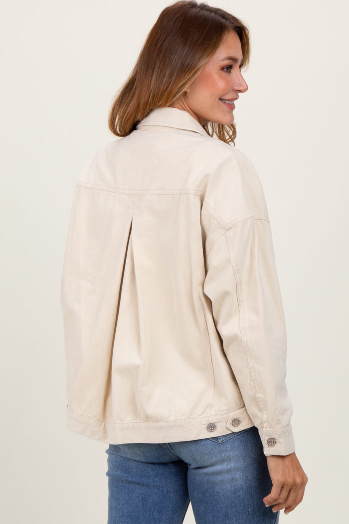 woman wearing a beige oversized jacket with a pleated back and button details, styled with blue jeans
