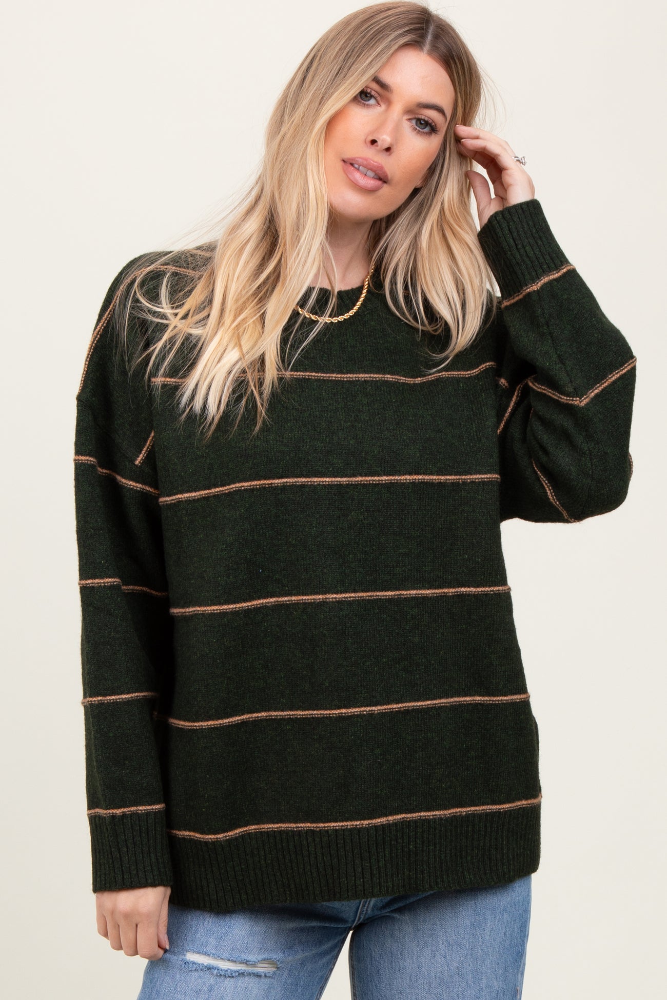 woman wearing a dark green striped sweater with beige lines and long sleeves paired with light blue jeans