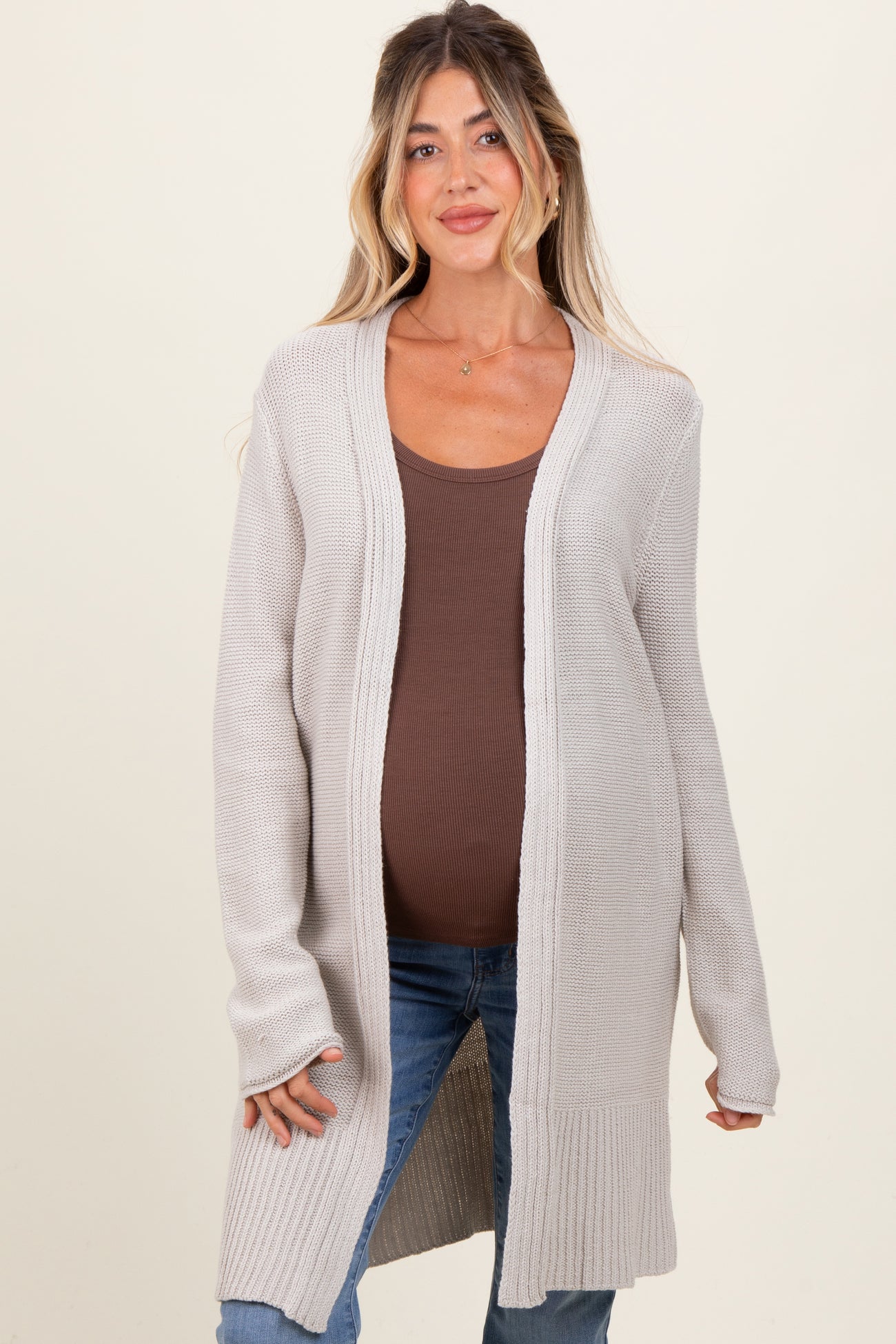 woman wearing a light gray long sleeve maternity cardigan over a brown fitted top and showing her baby bump