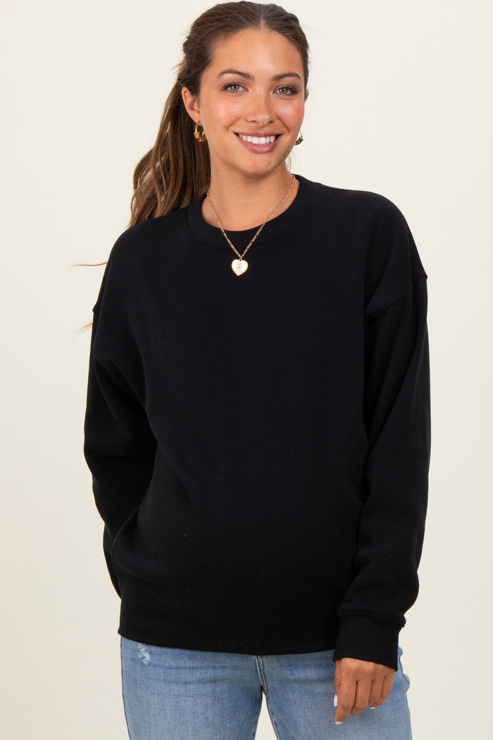 woman wearing a black oversized maternity sweatshirt and light blue jeans, smiling at the camera