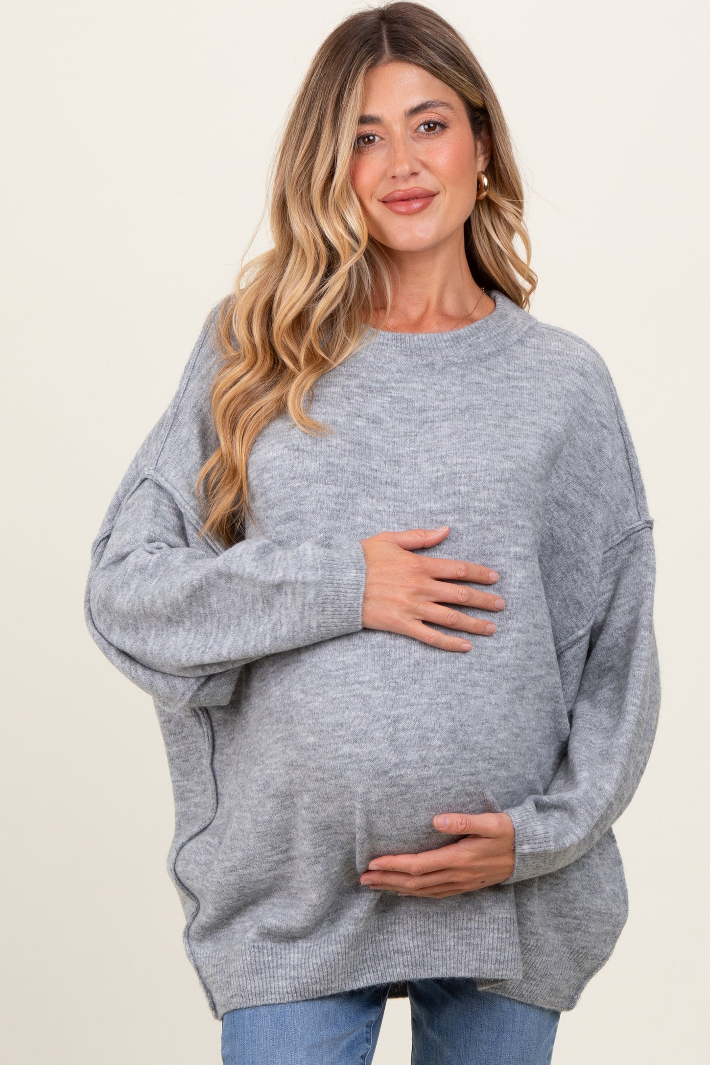 woman wearing a gray oversized maternity sweater and holding her baby bump
