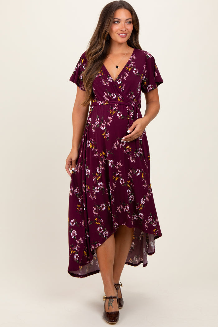 woman wearing a burgundy floral wrap maternity dress with flutter sleeves and a high-low hem, holding her baby bump