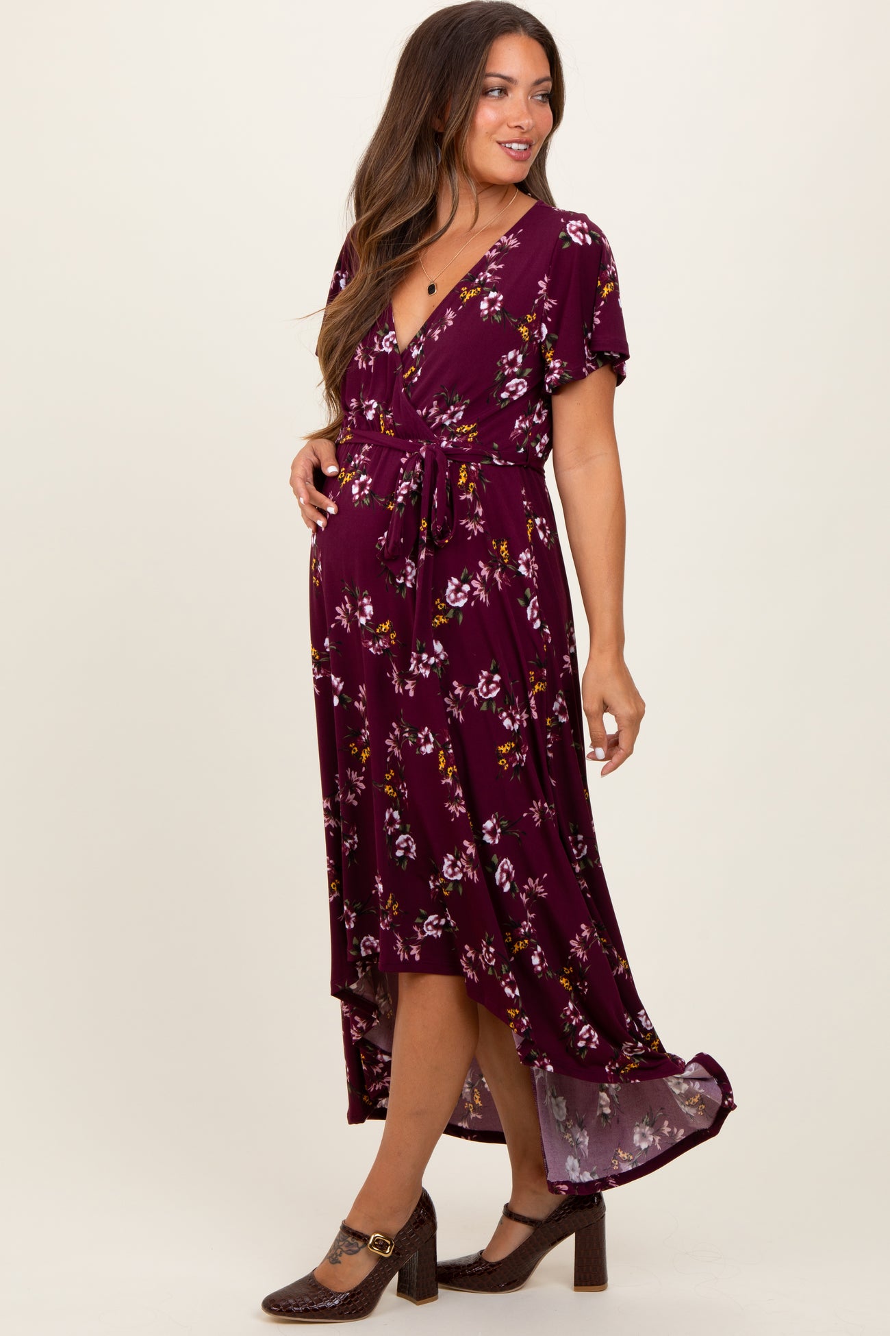 woman wearing a maroon floral maternity dress with a wrap style and a tie waist, showcasing a baby bump