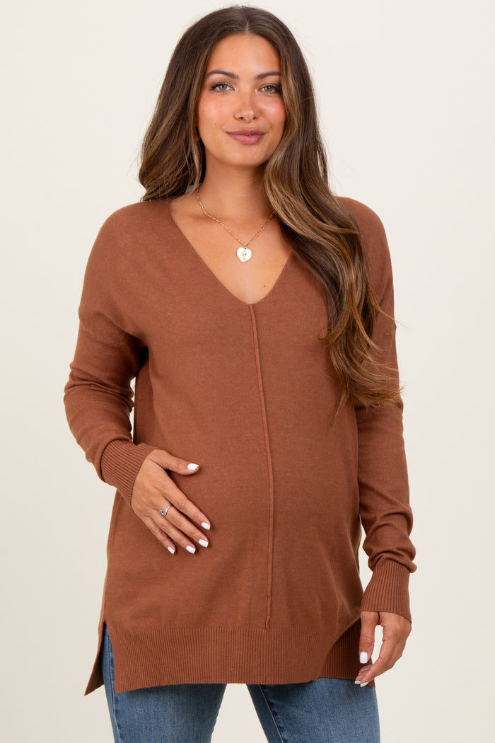 woman wearing a rust brown maternity sweater with a v-neck and side slits, showcasing her baby bump