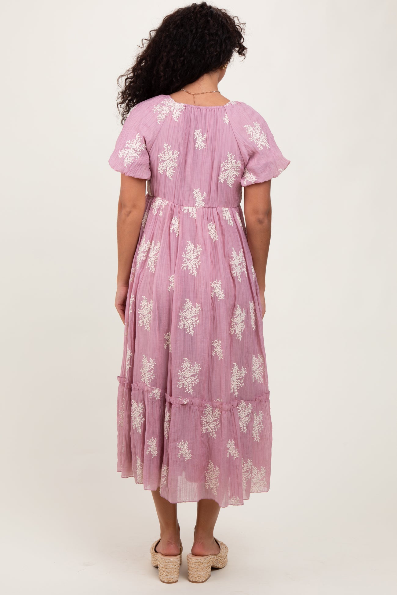 woman wearing a pink floral embroidered maxi dress with ruffled sleeves and tiered skirt from the back