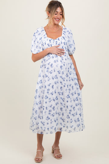 woman wearing a white floral maternity dress with puff sleeves and holding her baby bump