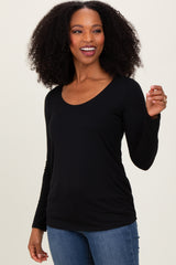 woman wearing a black long sleeve scoop neck top and blue jeans, smiling and posing with one hand raised