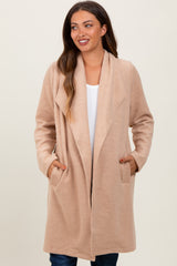 woman wearing a beige maternity wrap coat with pockets, styled open over a white top and denim jeans