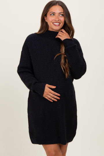 woman wearing a black maternity sweater dress with long sleeves and a high neckline, holding her baby bump