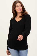 woman wearing a black ribbed long sleeve top with a v-neck and balloon sleeves, smiling and posing with one hand raised