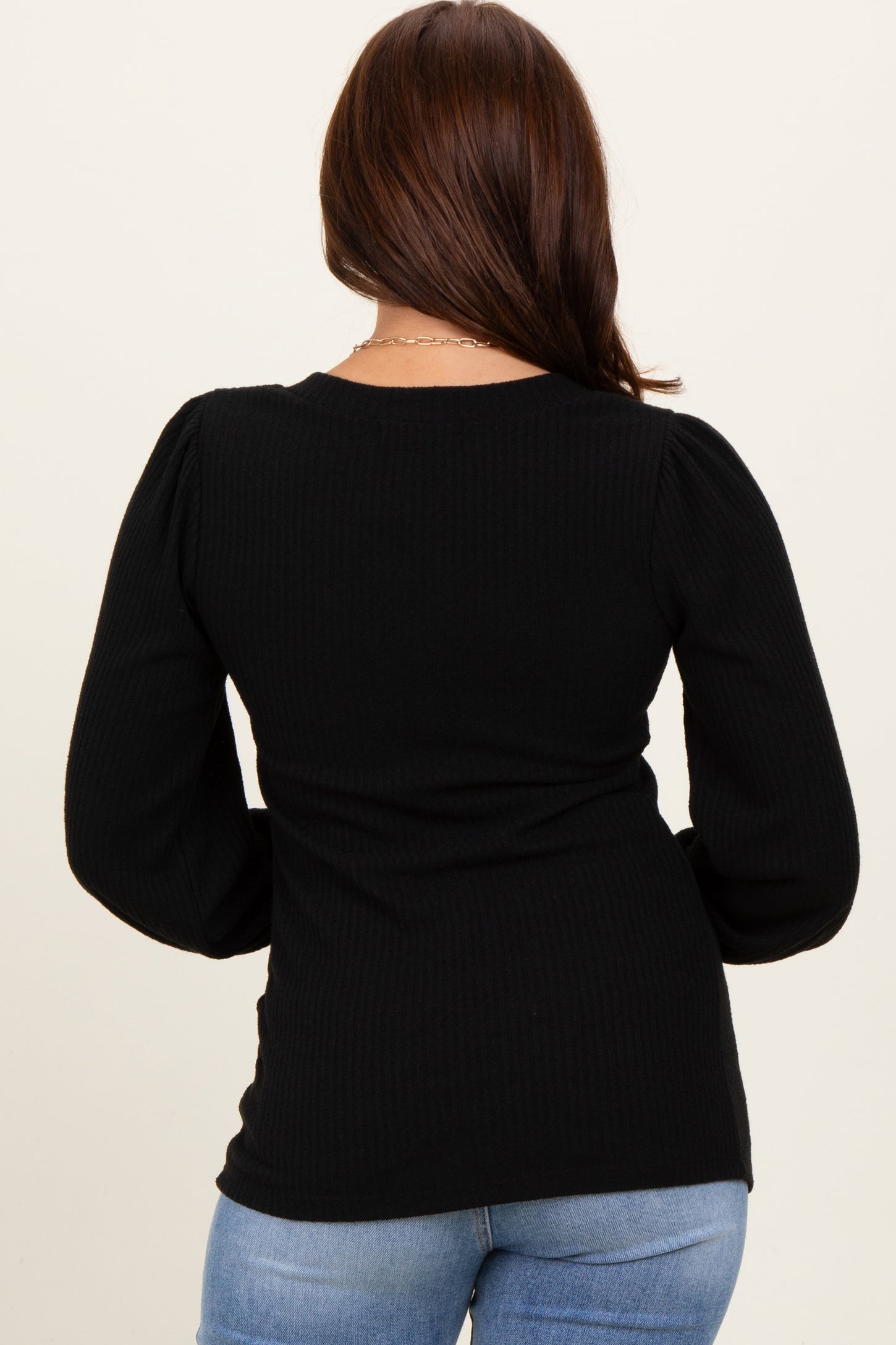 woman wearing a black ribbed long sleeve top with puff sleeves, viewed from the back