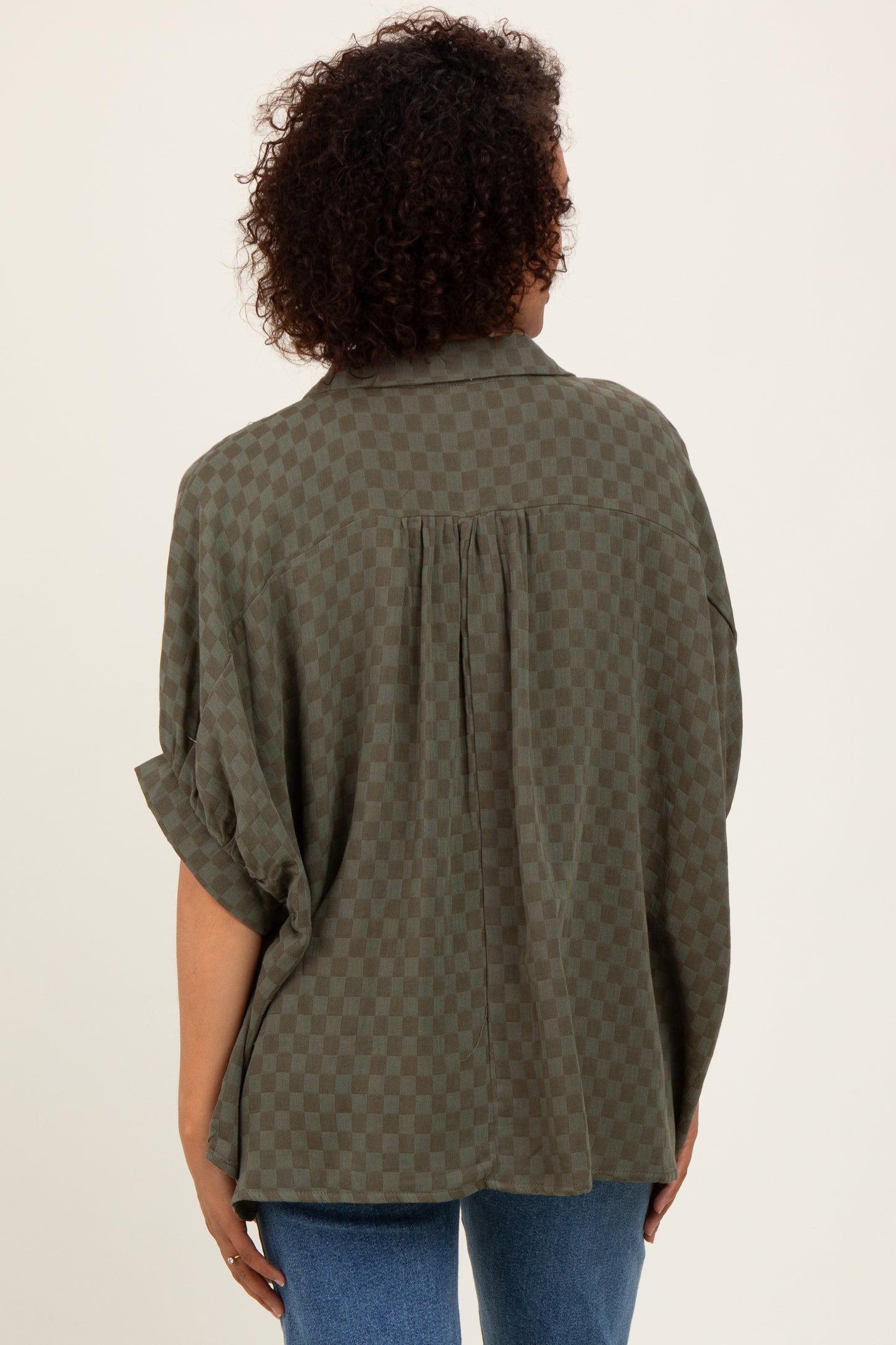woman wearing an olive green checkered oversized button-up shirt with a pleat detail on the back