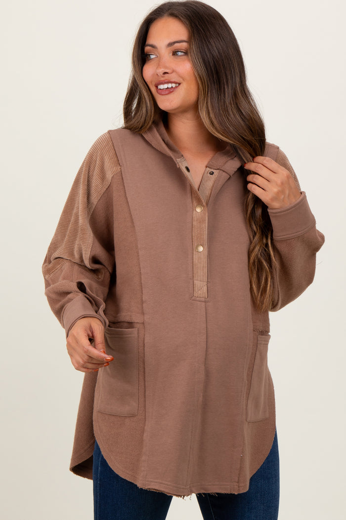 woman wearing a brown maternity hoodie with buttons and side pockets, smiling and showing her baby bump