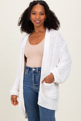 woman wearing an open front white knit cardigan over a beige tank top and high-waisted jeans