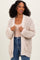 woman wearing a beige chunky knit cardigan with pockets over a beige top and blue jeans