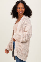 woman wearing a chunky beige knit cardigan over a light top and denim jeans, smiling and posing to the side