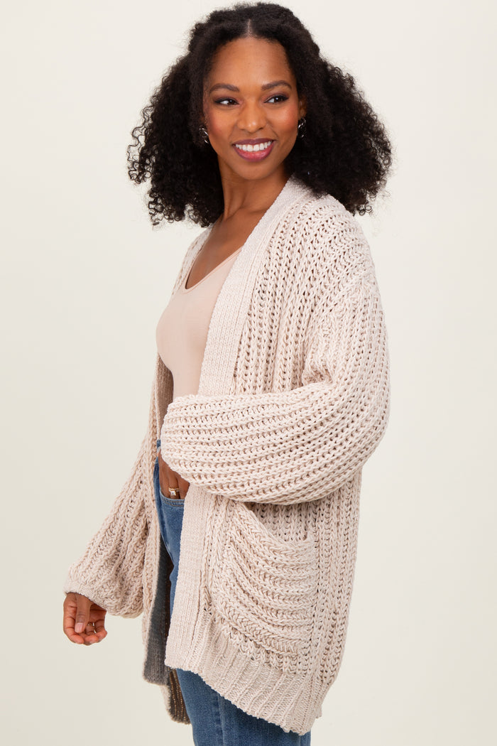 woman wearing a chunky beige knit cardigan over a light top and denim jeans, smiling and posing to the side