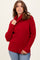 woman wearing a bright red knitted sweater with a cowl neck and side slits, paired with blue jeans