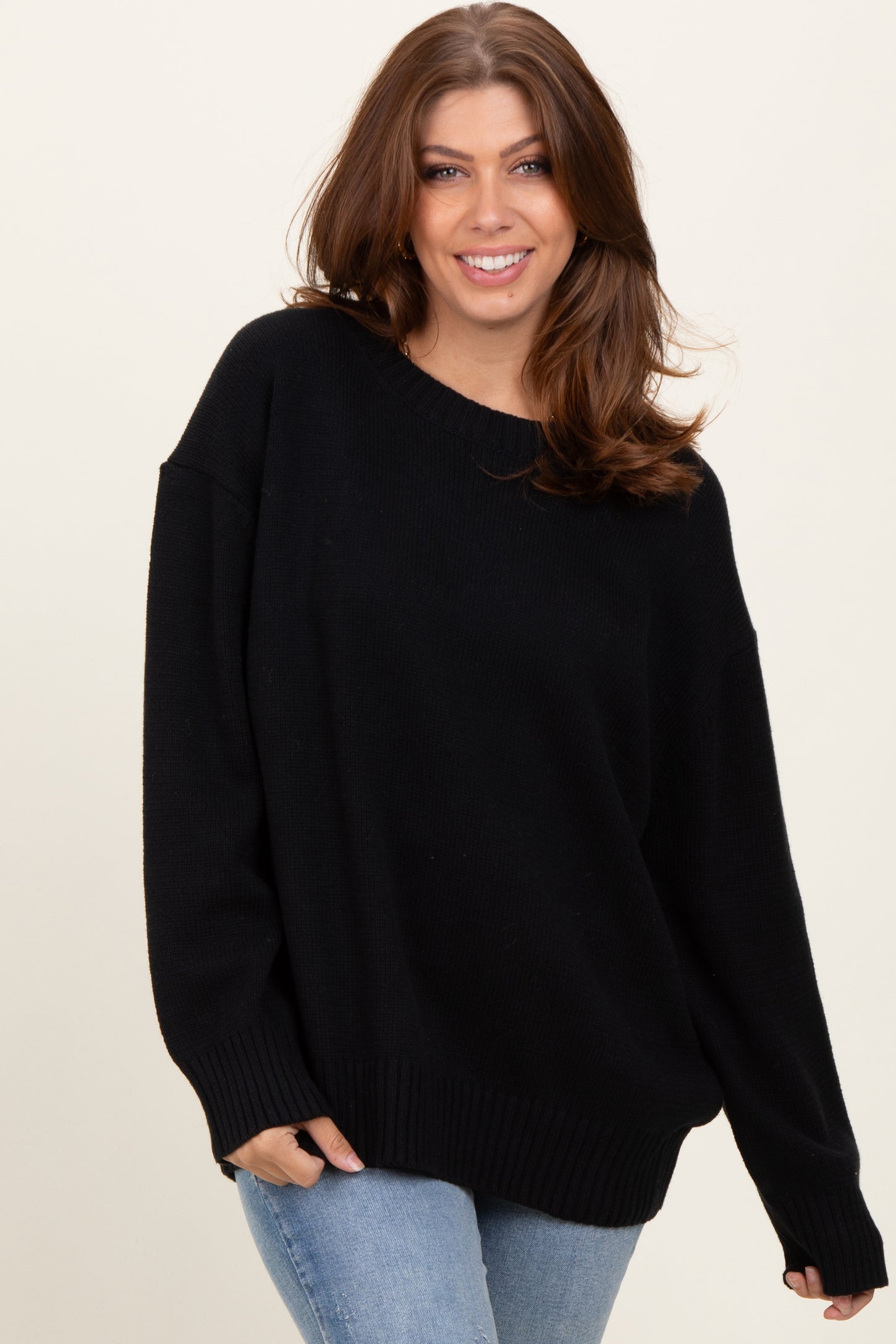 woman wearing an oversized black sweater with a ribbed hem and long sleeves, paired with blue jeans