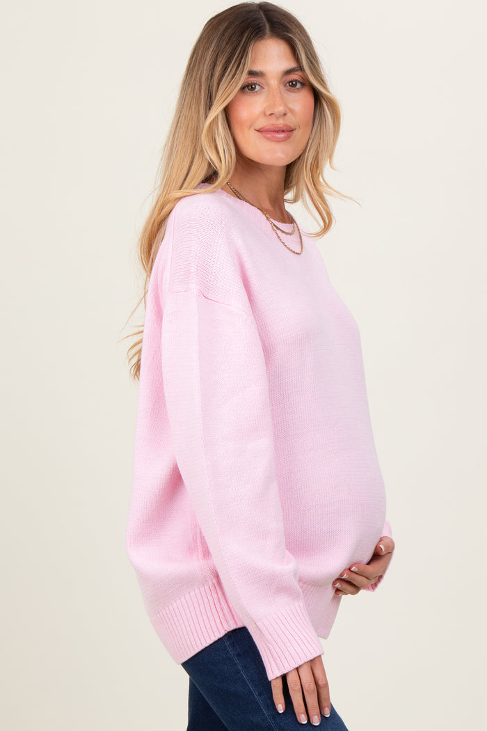 woman wearing a light pink oversized maternity sweater and holding her baby bump