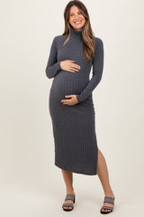 woman wearing a dark gray maternity dress with a turtleneck and side slit, holding her baby bump