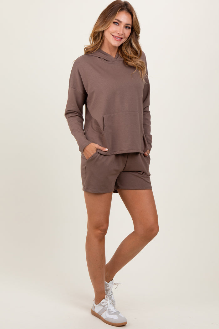 woman wearing a brown long sleeve hoodie with a pocket and matching shorts, standing with hands in pockets
