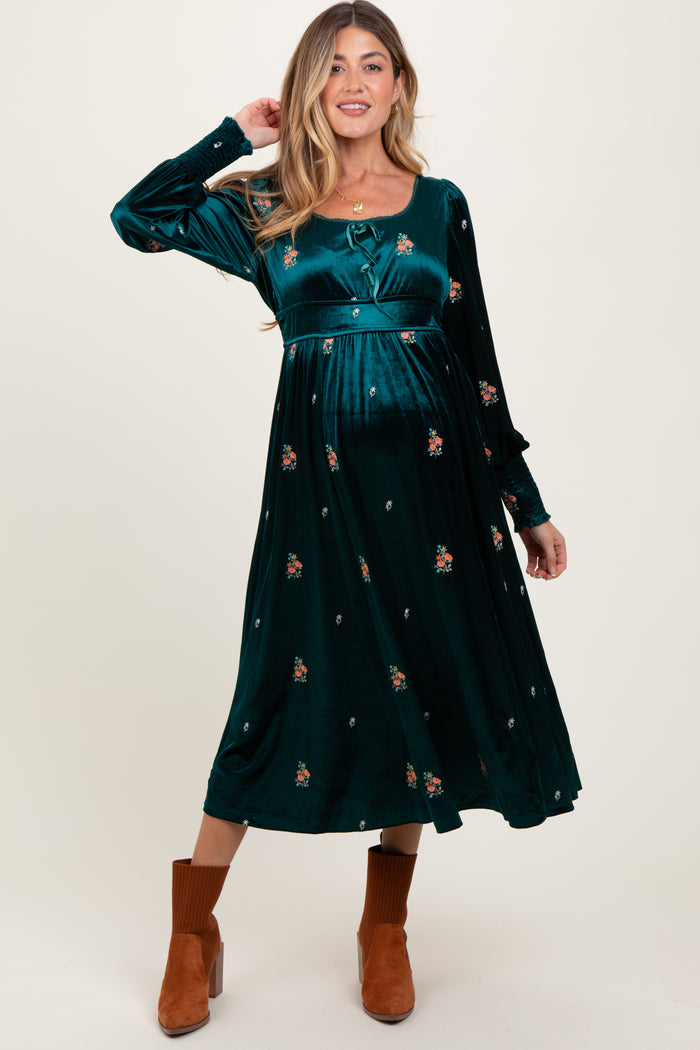 woman wearing a green velvet maternity dress with floral embroidery and long sleeves, featuring a flowy silhouette and baby bump