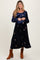 woman wearing a navy blue long sleeve maternity dress with floral embroidery and holding her baby bump