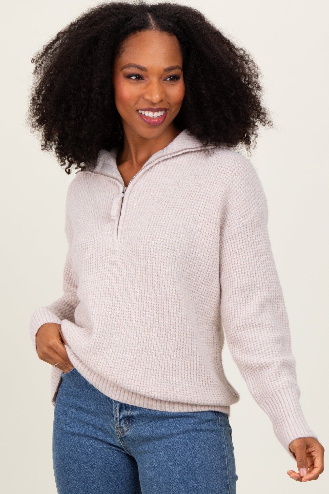 woman wearing a light pink pullover sweater with a hood and half-zip fastening, styled with blue jeans