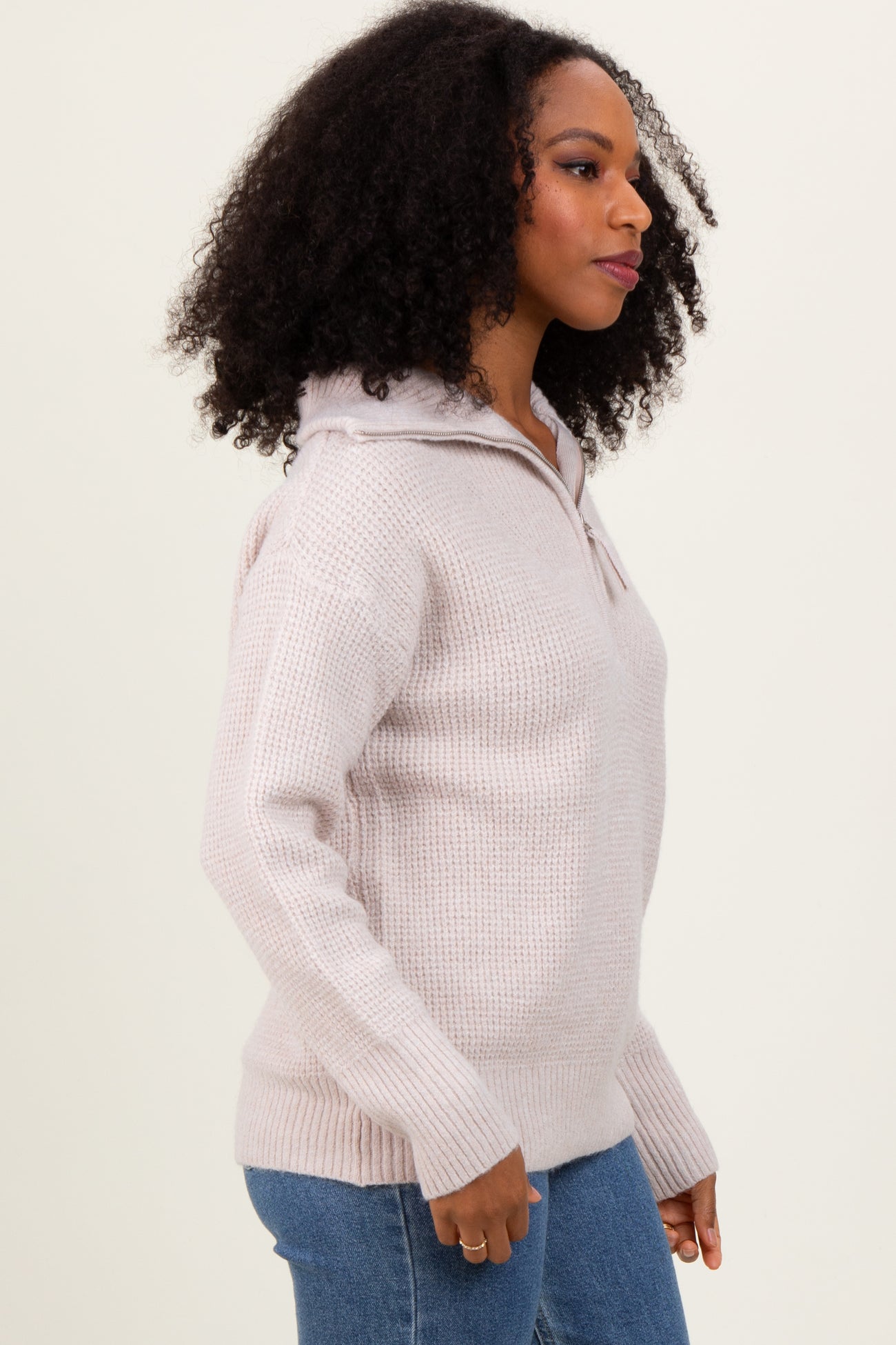woman wearing a light pink hooded sweater with a half zip, styled with blue jeans