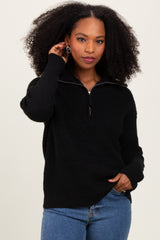 woman wearing a black zip-up sweater with a textured finish and blue jeans.