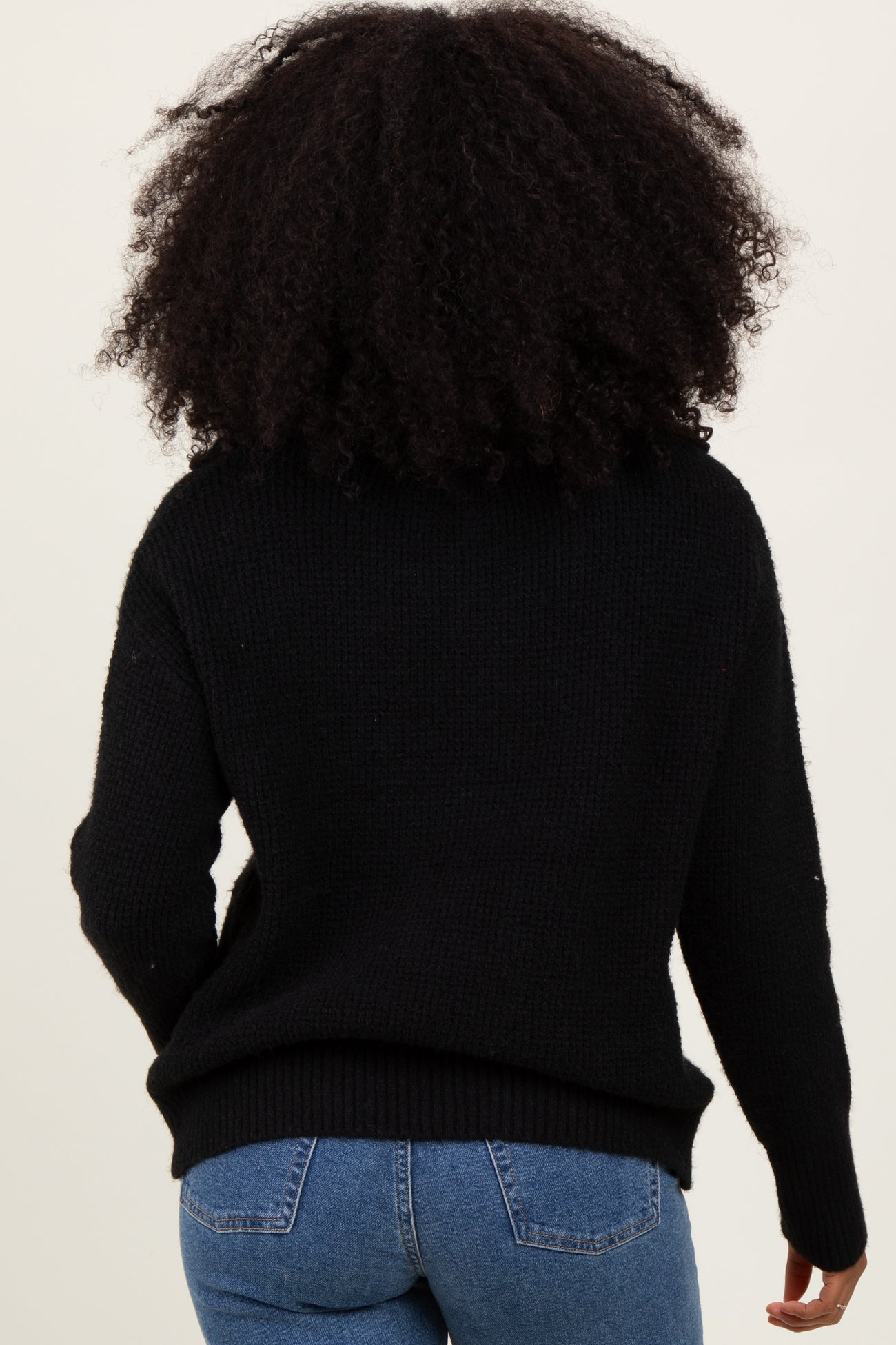 woman wearing a black oversized knit sweater, seen from the back, paired with blue jeans